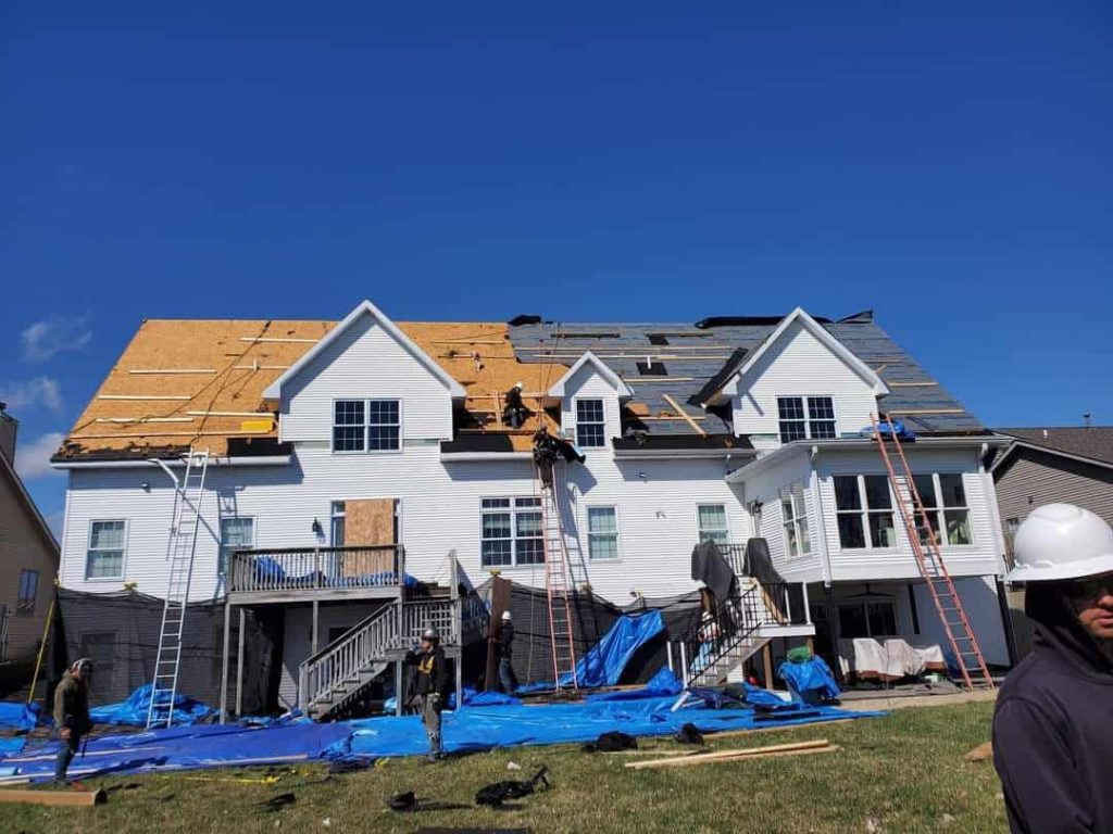 Roof repair in progress on a sunny day with workers on the roof and equipment on the ground.